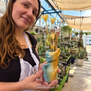 משתתפת מחזיקה אגרטל בטון בצורת פנים ופלג גוף בגווני טורקיז וזהב עם פרחים יבשים