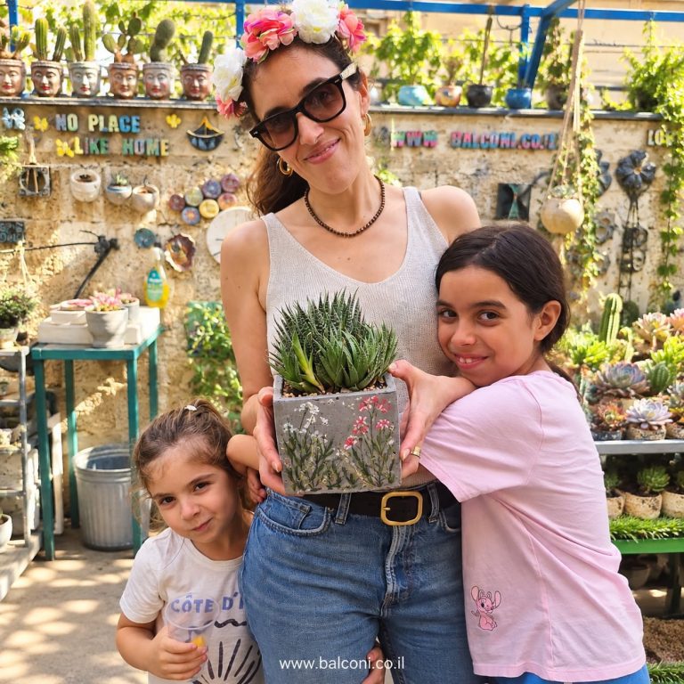 אם ושתי בנותיה מחבקות עציץ בטון מרובע מצויר עם סוקולנטים בסטודיו