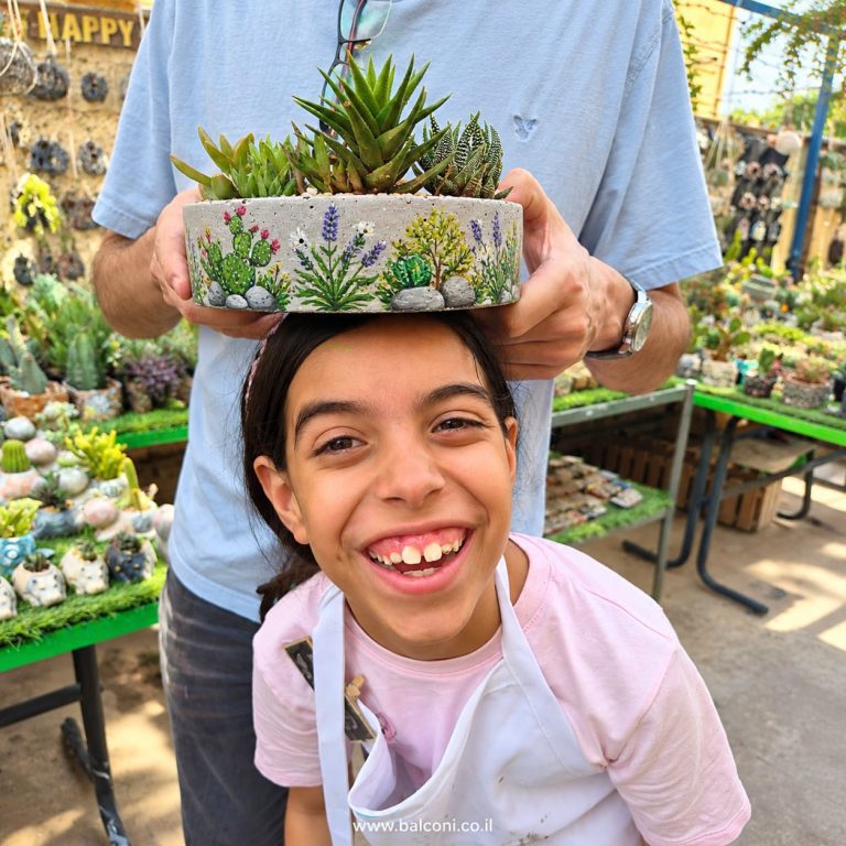 ילדה צוחקת כשמעל ראשה אדנית בטון מצוירת מלאה סוקולנטים